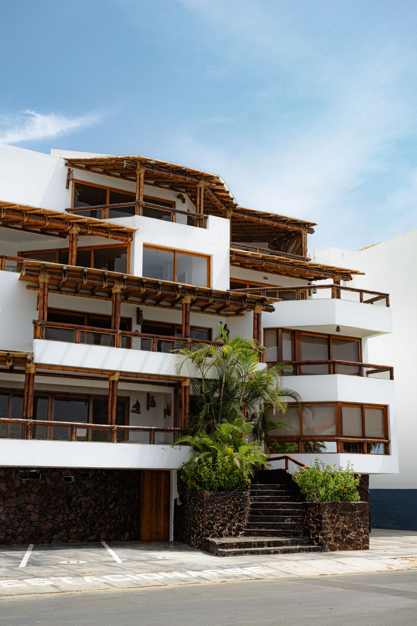Fotografía de edificio residencial blanco con balcones de madera y vegetación tropical